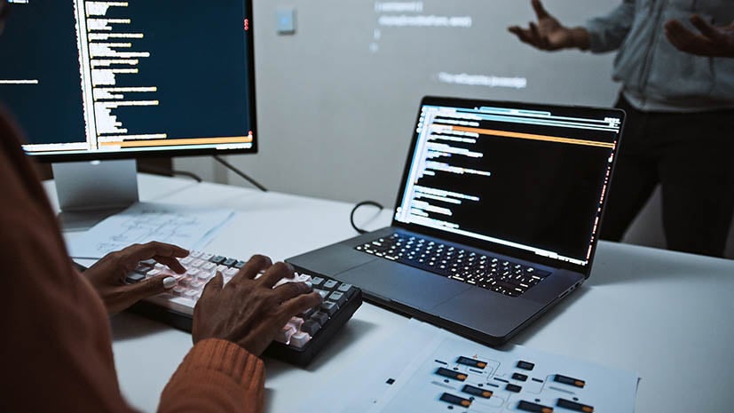 view of professor in front with code on white board and back view of a student with code on laptop