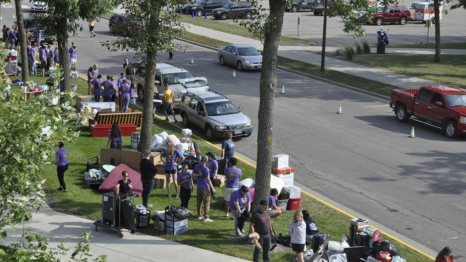 Dorm move in rush, with group of people carrying things from cars to the dorms