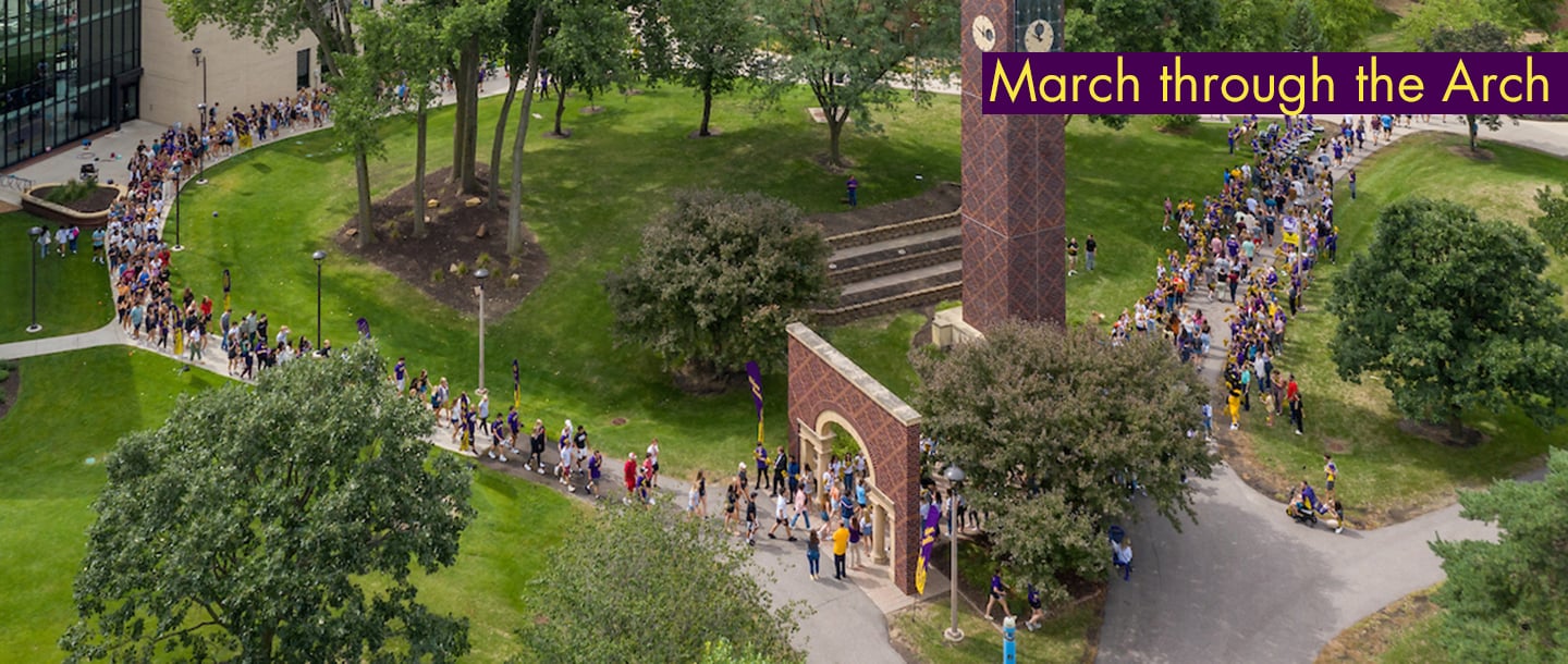 Students marching through the arch by the clock tower on campus