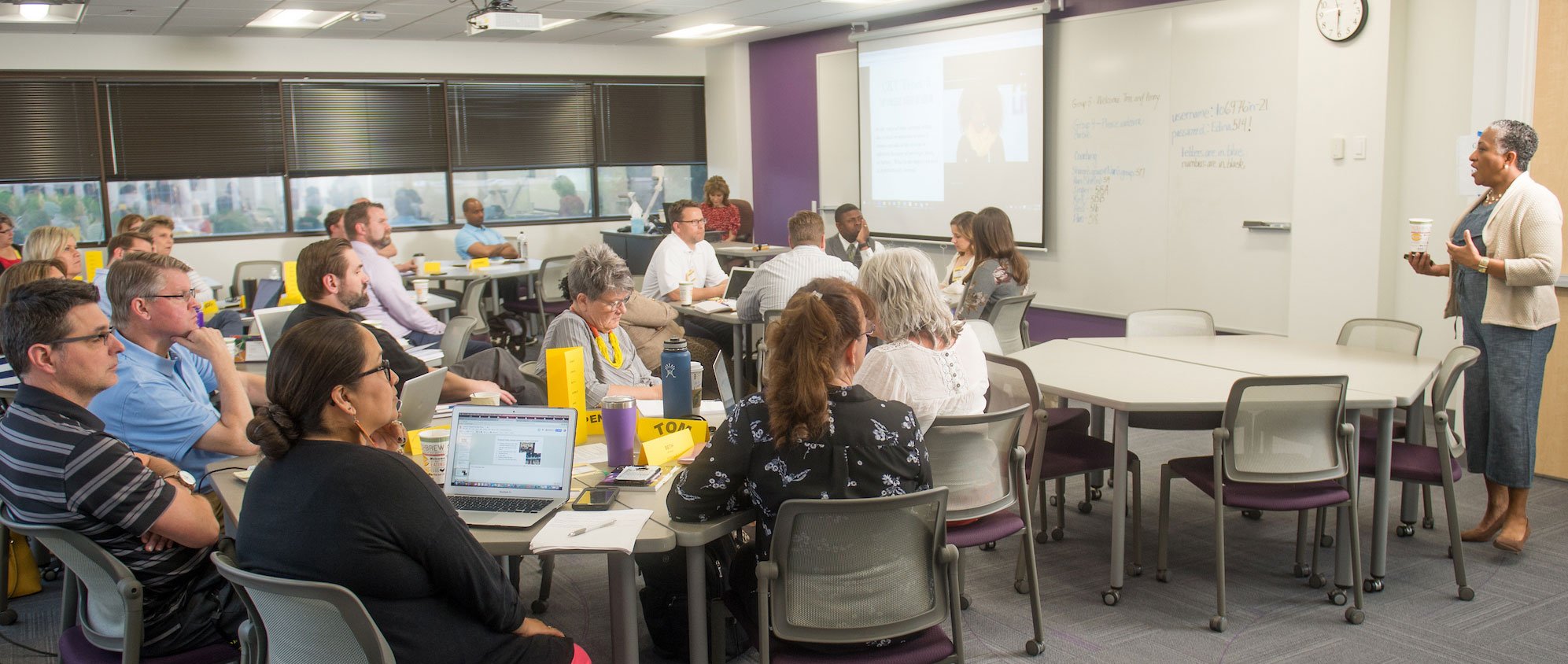 a group of students in a classroom with laptops and a projector screen