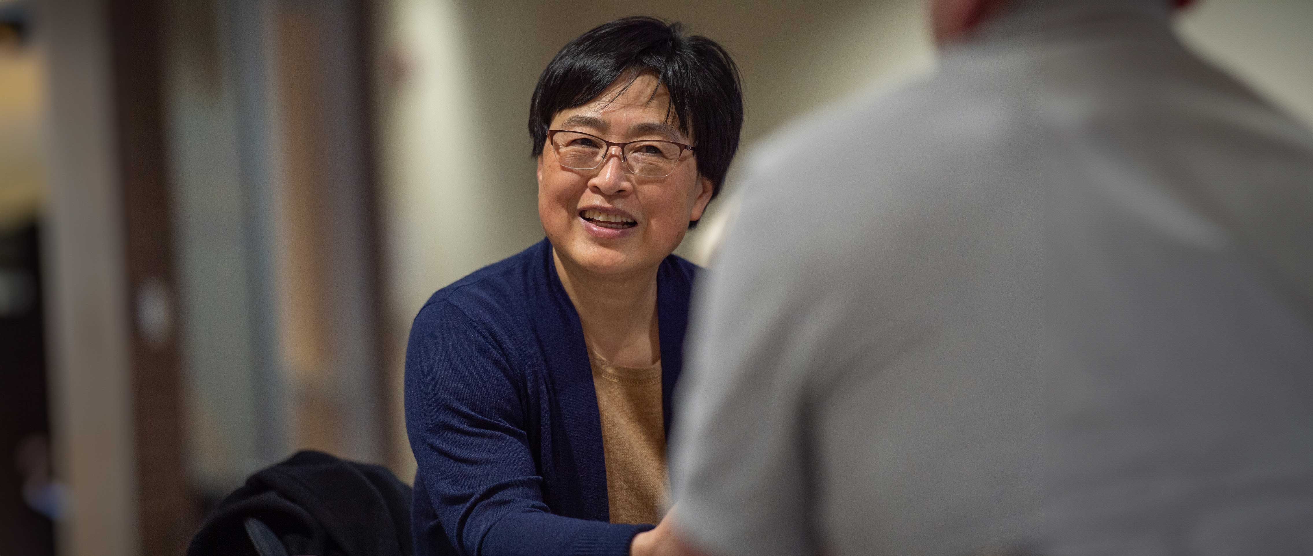 a person with glasses, sitting down at a table and talking with a another person