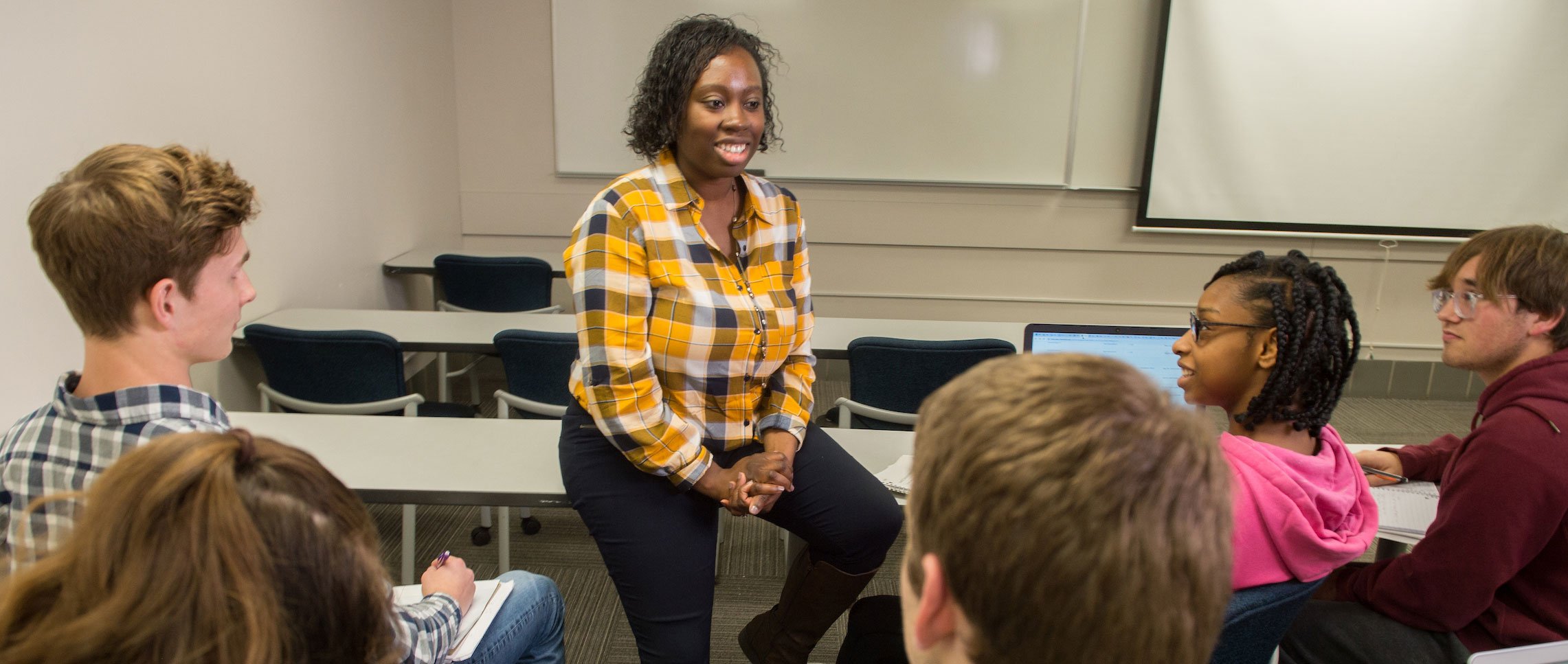 a faculty sitting in front of a group of students and talking to them