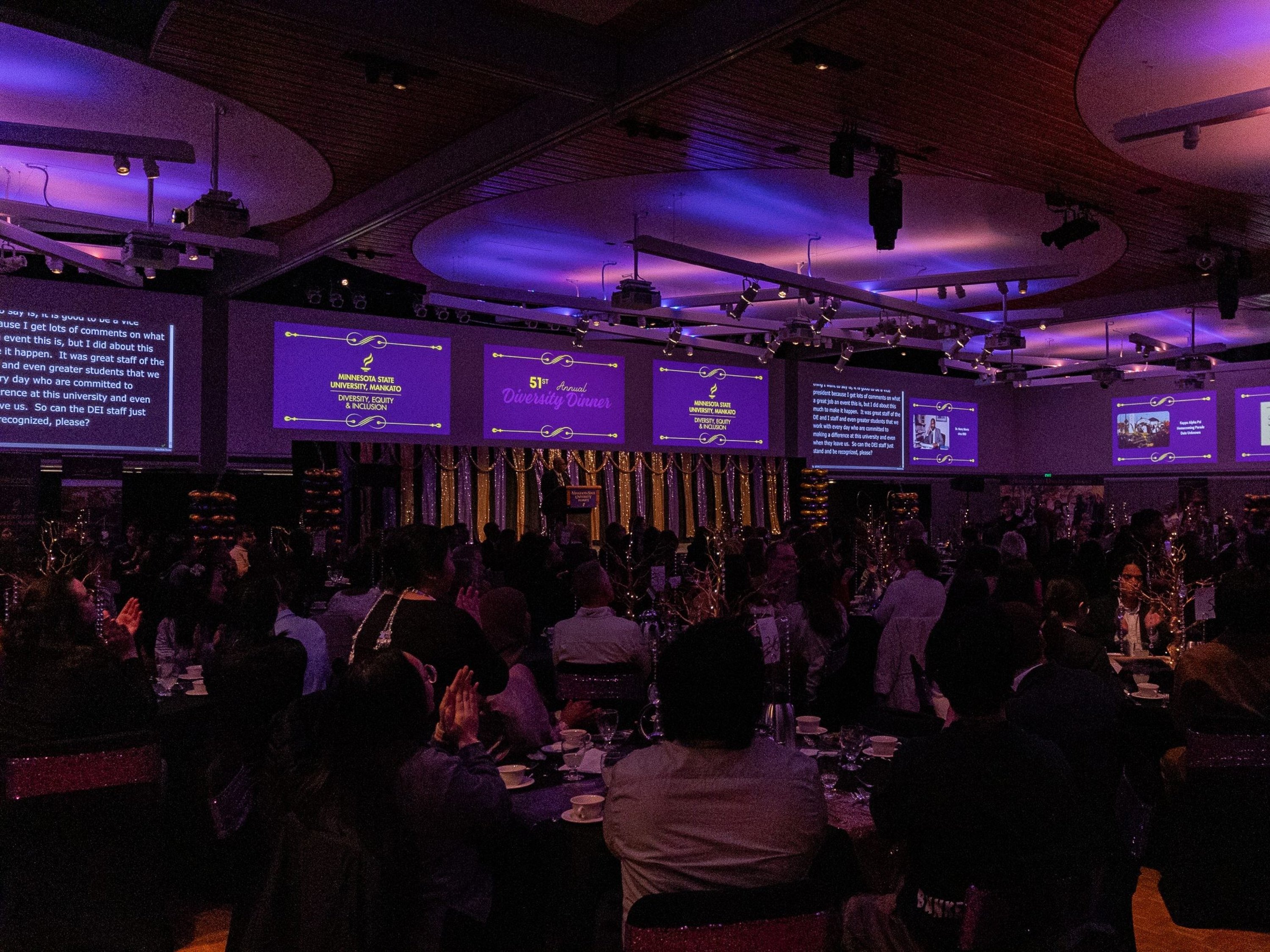 a group of people sitting at tables in a room with a large screen