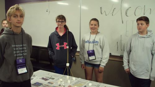 ETS students in a classroom posing around a sculpture made from sticks and marshmellows