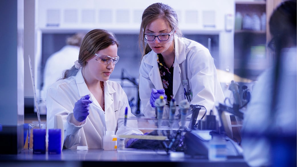 Two female students with white coats working with samples in a science lab 