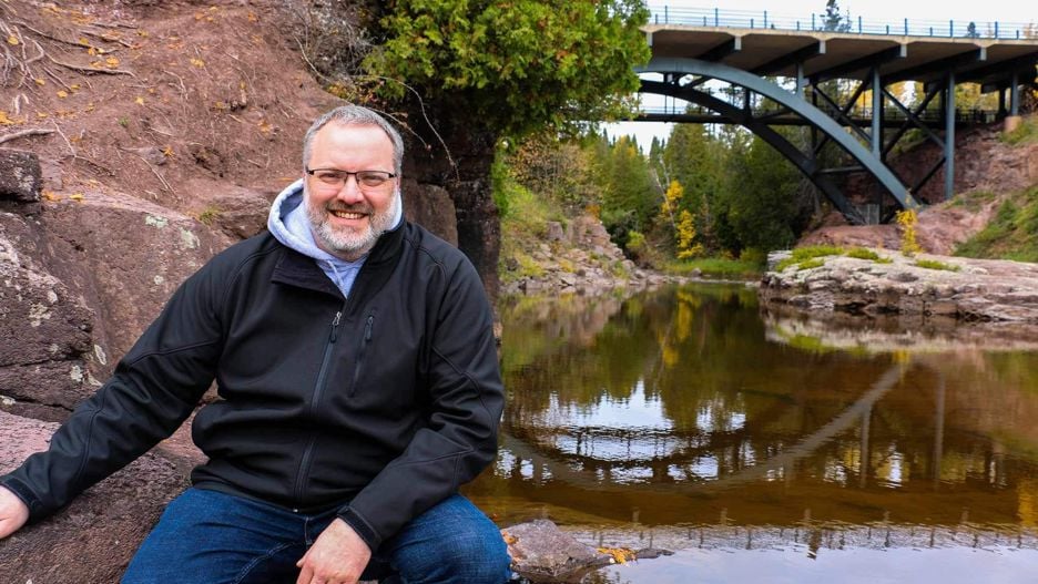 Richard Kuttner posing outside with a smile next to a river in his hometown of Hutchinson, Minnesota