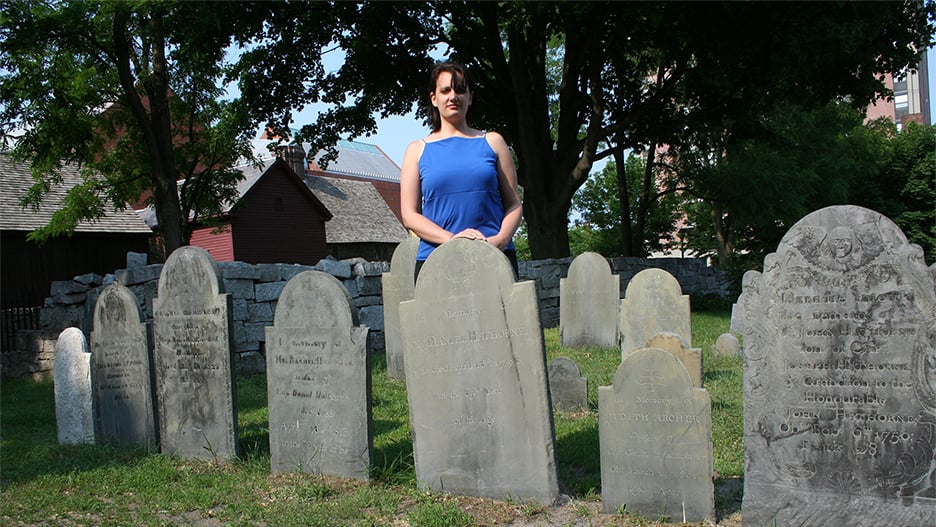 Professor Beth Heidelberg posing outside behind some tomb stones at an old cemetery