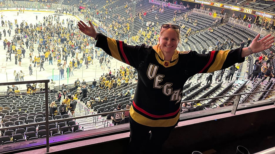 Former Maverick hockey player Sheri Hudspeth posing on the top row of the stadium with her arms extended as the National Hockey League’s Vegas Golden Knights and fans gather on the ice