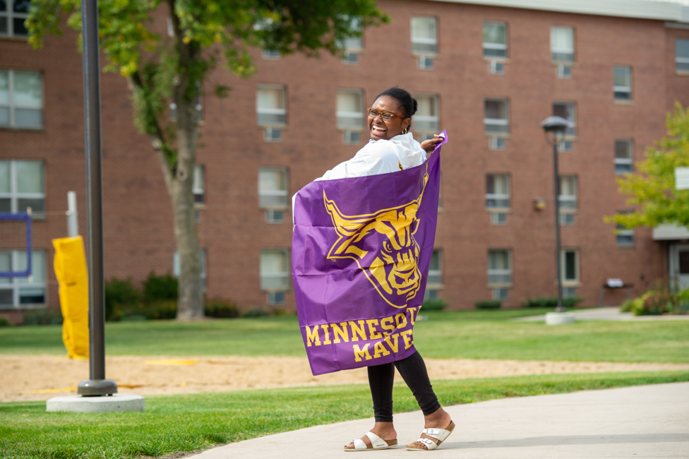 Student wrapped around an MSU Maverick flag, smiling.